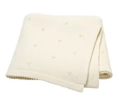 Couverture de naissance pour bébé en maille tricotée douce de couleur écrue, présentant un motif délicat de petits points ajourés répartis sur toute la surface et des bords travaillés.