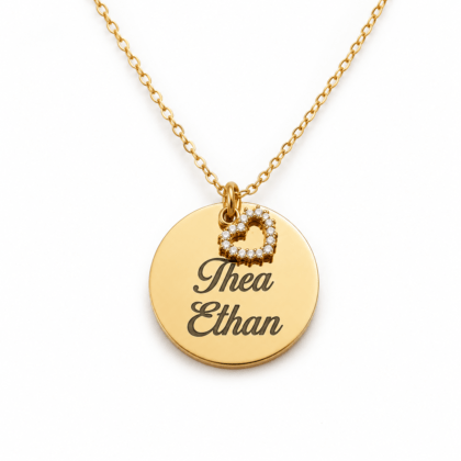 Collier délicat en métal doré pour femme, composé d'une fine chaîne et d'un pendentif médaille circulaire lisse gravé des prénoms "Thea Ethan", accompagné d'un petit cœur ajouré incrusté de strass.