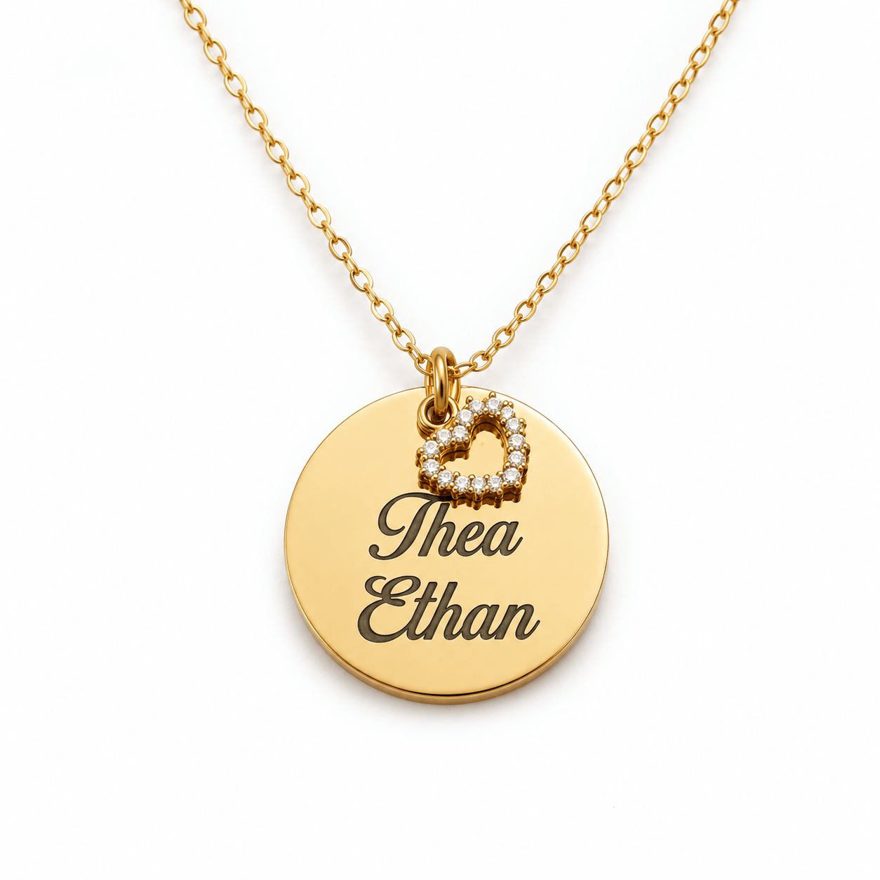 Collier délicat en métal doré pour femme, composé d'une fine chaîne et d'un pendentif médaille circulaire lisse gravé des prénoms "Thea Ethan", accompagné d'un petit cœur ajouré incrusté de strass.