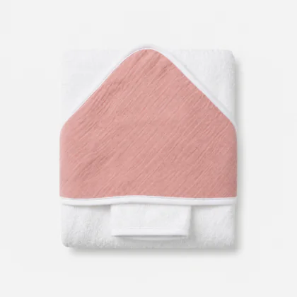 Cape de bain pour bébé pliée, réalisée en tissu éponge blanc doux avec une capuche triangulaire ornée d'un détail en mousseline de couleur vieux rose.
