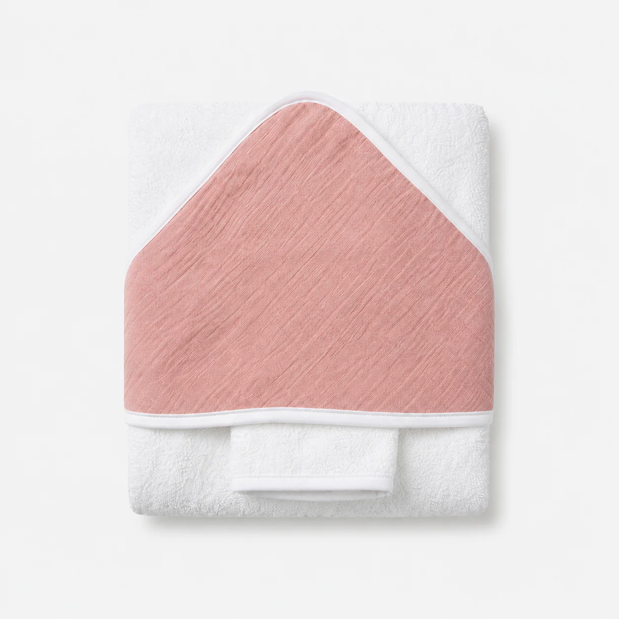 Cape de bain pour bébé pliée, réalisée en tissu éponge blanc doux avec une capuche triangulaire ornée d'un détail en mousseline de couleur vieux rose.